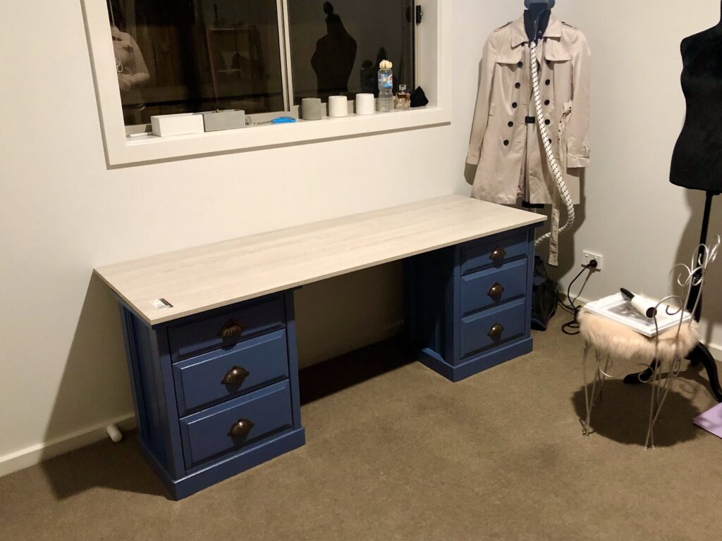 A blue desk with white top and drawers in a room, accompanied by a mannequin and a coat on a hanger.